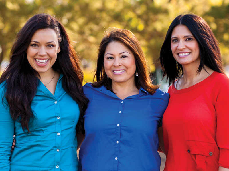 A group of three lady friends smiling in the outdoors.